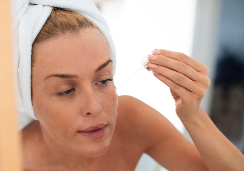 Woman with her hair wrapped in a towel applying serum to her forehead with a glass dropper