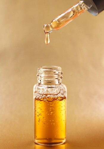 Dropper releasing a bead of golden serum above an open glass bottle