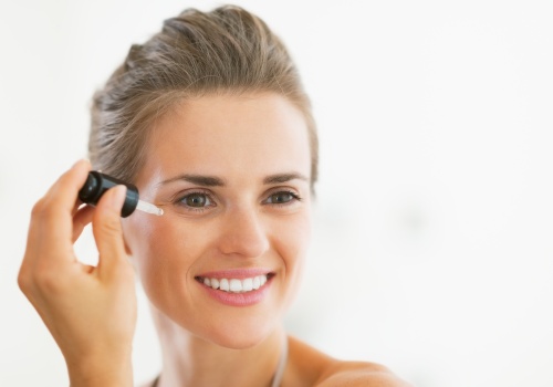 Smiling woman applying facial serum beside her eye with a glass dropper