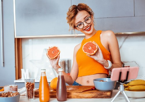 Woman holding grapefruit halves beside a juicer and a phone on a kitchen counter