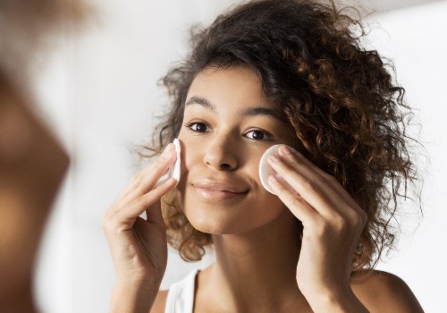 Woman cleansing both cheeks with cotton pads while looking in a mirror