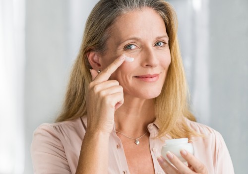 Woman dabbing cream beneath her eye while holding an open skincare jar