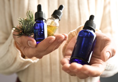 Hands holding blue and clear essential oil bottles beside a leafy sprig
