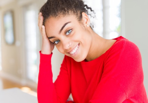 Smiling woman in a red top with one hand resting against her temple
