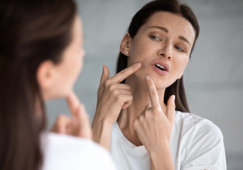 Woman examining a spot on her chin in a bathroom mirror