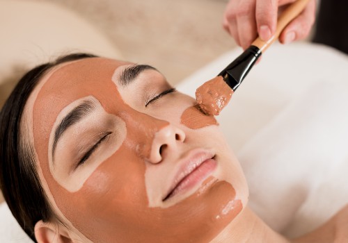 Facial mask being brushed onto a reclining woman's cheek during a spa treatment