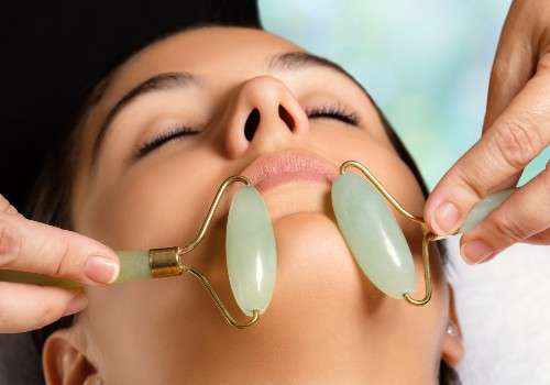 Two green jade rollers being used to massage a reclining woman's chin and jawline