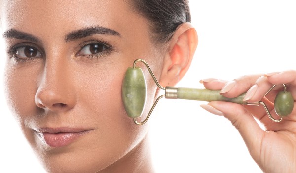 Woman holding a double-ended green jade roller against her cheek