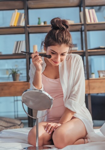 Woman seated in a bathroom checking her face in a round tabletop mirror