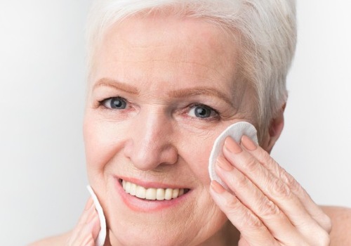 Woman with short white hair wiping her cheek with a cotton pad