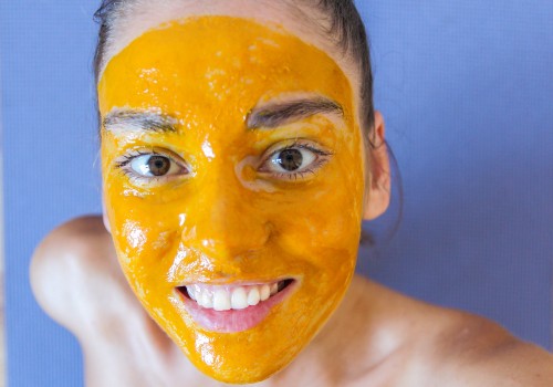 Smiling woman wearing a bright yellow facial mask against a blue background