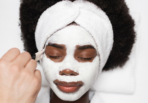 Woman with her hair in a towel using a brush to apply a white facial mask