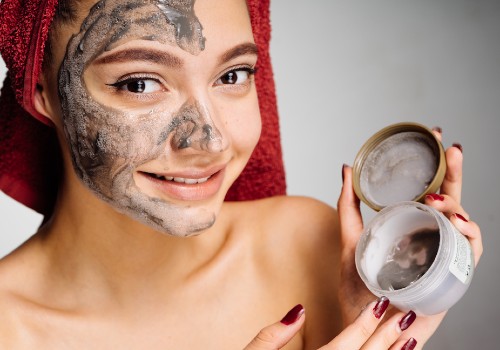 Woman wearing a gray clay mask and holding an open jar of the mask beside her face