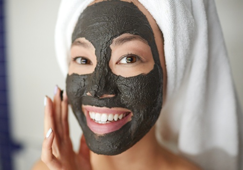 Smiling woman wearing a black clay mask with the areas around her eyes and mouth left uncovered