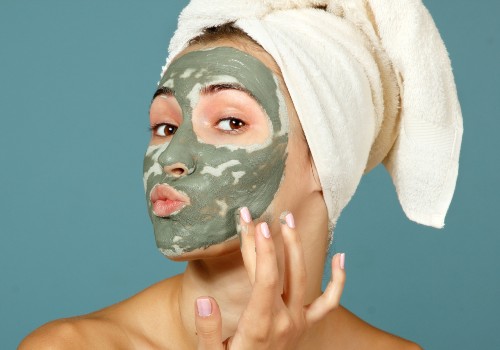 Woman with her hair in a towel touching the green clay mask on her cheek