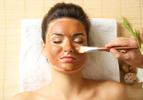 Practitioner brushing a golden facial mask onto a woman's cheek as she reclines with her eyes closed