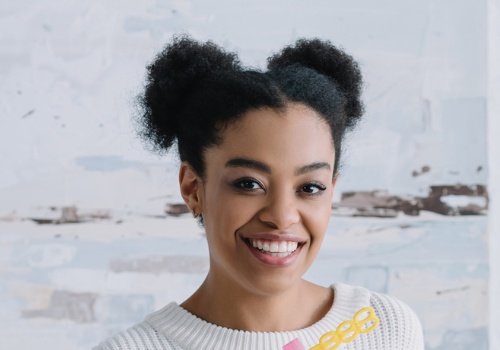 Smiling woman with her hair in two puffs against a white brick wall