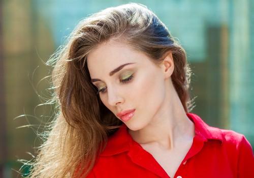 Woman in a red shirt looking down outdoors, with her hair swept to one side