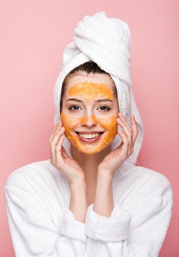 Smiling woman with a towel around her hair and an orange facial mask on her skin