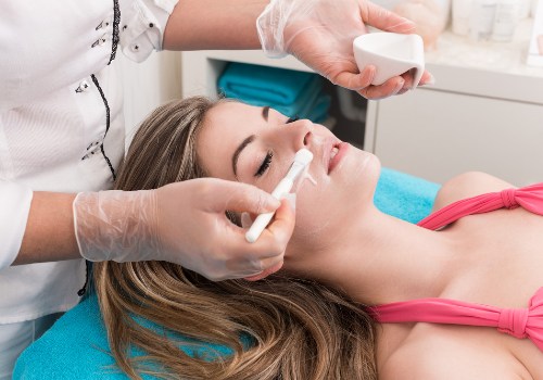 Practitioner brushing a facial treatment across a reclining woman's nose and cheek