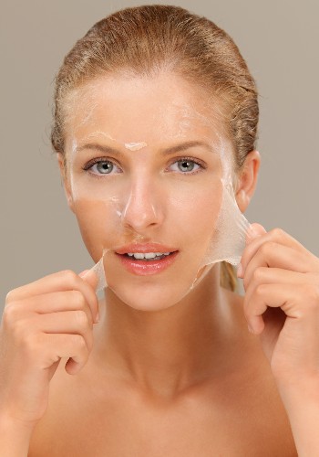 Woman lifting a transparent peel-off facial mask away from both cheeks