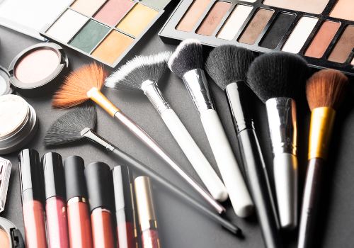 Makeup brushes, eye shadow palettes, face powders, and lip products arranged on a dark surface