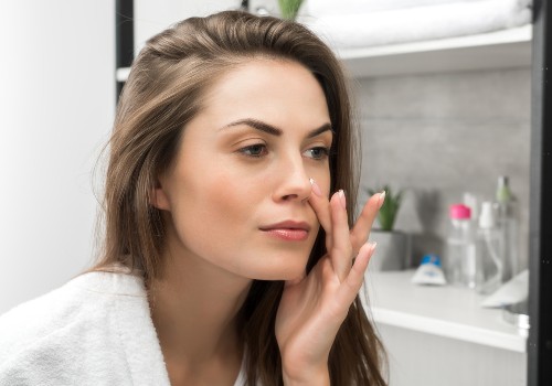 Woman touching her cheek while examining her face in a bathroom mirror