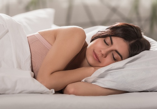 Woman sleeping on her side with her head on a white pillow beneath white bedding