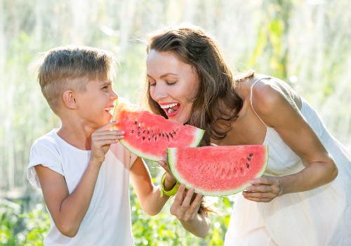 Woman and child eating large watermelon slices together outdoors