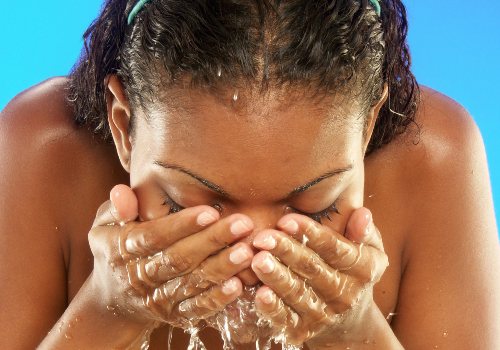 Woman splashing water onto her face with both hands against a blue background