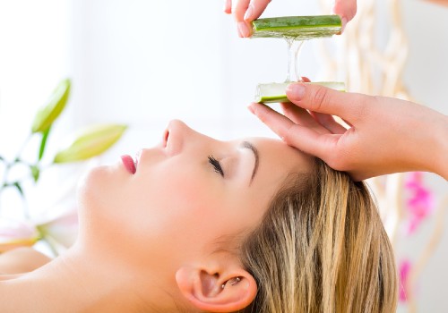 Fresh aloe vera gel being squeezed from a cut leaf above a reclining woman's forehead