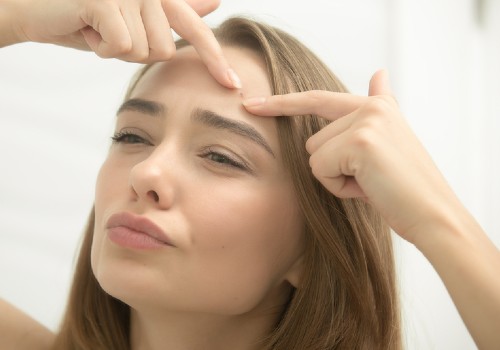 Woman pressing her fingertips around a spot on her forehead while looking in a mirror