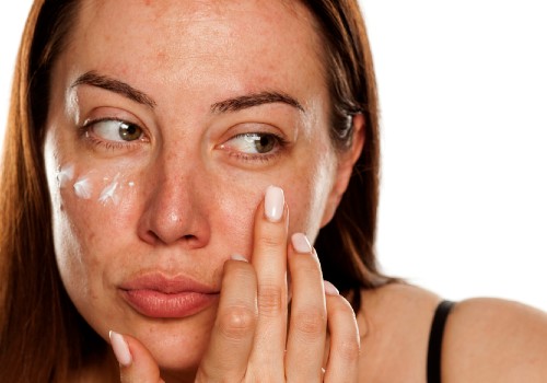 Woman dabbing white face cream onto her cheeks with her fingertips