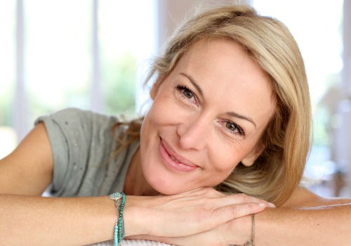 Smiling woman resting her head on her folded hands beside a window
