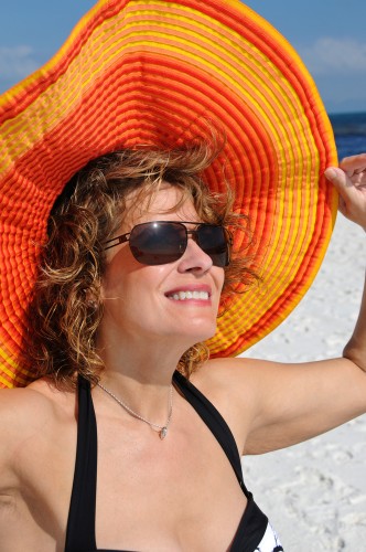 Woman wearing sunglasses and a wide orange sunhat on a sunny beach