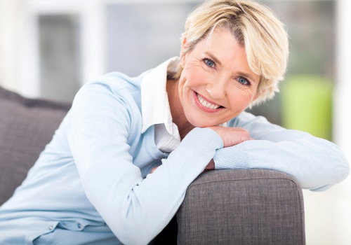 Smiling woman with short blonde hair leaning on the arm of a gray sofa