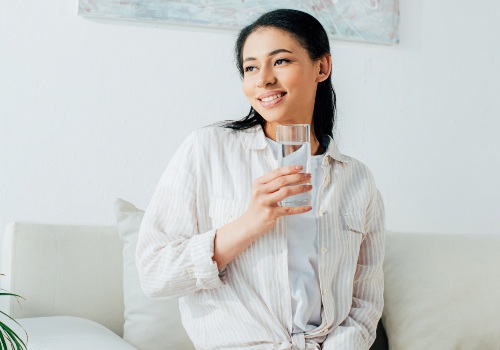 Woman holding a glass of water while sitting on a sofa and looking to one side