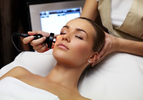 Handheld red light device being applied to a reclining woman's cheek during a facial treatment