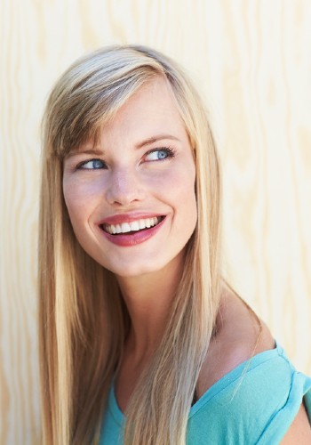 Smiling woman with long blonde hair looking to one side beside a light-colored wall
