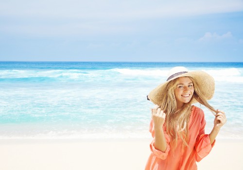 Woman holding the brim of a wide sunhat while standing beside turquoise ocean water
