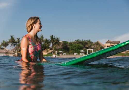 Woman standing in the ocean beside a green surfboard near a palm-lined shore