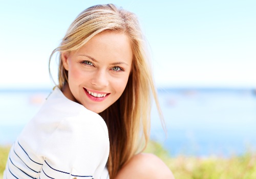 Smiling blonde woman looking back over her shoulder beside the sea