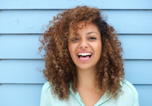 Woman with curly hair laughing in front of a blue wooden wall
