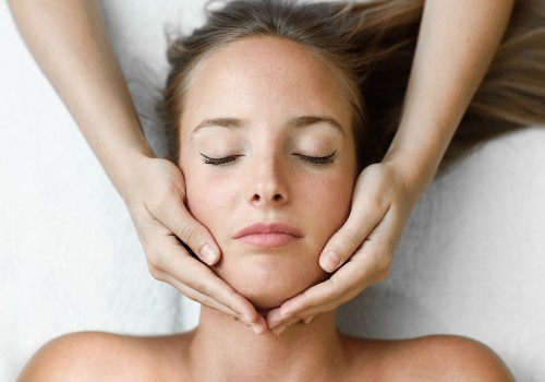 Hands cradling and massaging a reclining woman's jawline while her eyes are closed