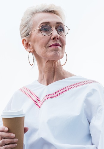 Older woman wearing round glasses and hoop earrings while holding a takeaway cup