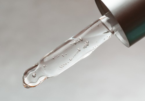 Close-up of a glass skincare dropper holding clear serum with a droplet at its tip