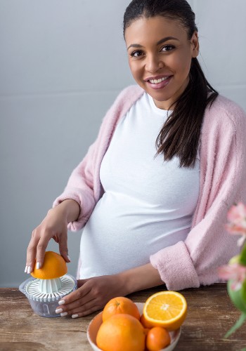 Woman pressing an orange half onto a manual citrus juicer at a kitchen table