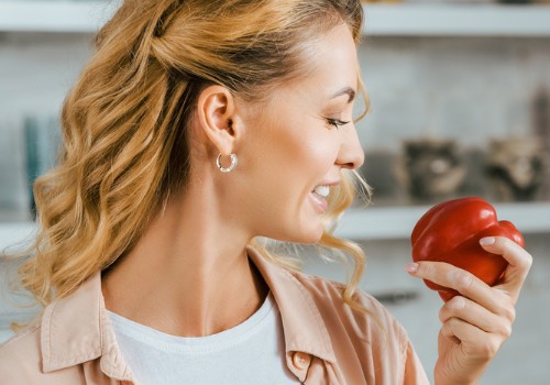 Woman smiling while holding a red apple near her face in a kitchen