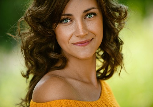 Portrait of a smiling woman with curly brown hair and a yellow top outdoors