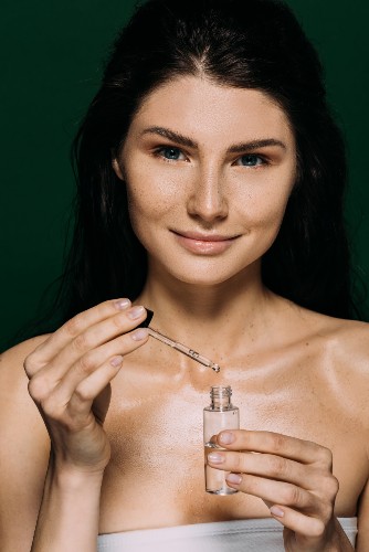 Woman holding a small glass skincare bottle and a dropper against a dark background